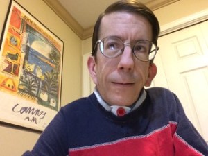 Image Description: Selfie photo of a white man with short brown hair and glasses. He has a visible tracheostomy.