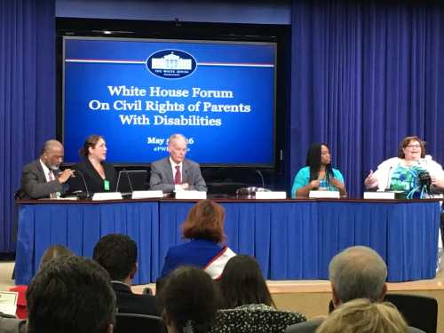 Five individuals sitting behind a draped table in front of a screen that reads "White House Forum on Civil Rights of Parents with Disabilities". At the end of the table is a brunette haired woman sitting in a wheelchair and speaking passionately. Photo courtesy of Rebecca Cokley.