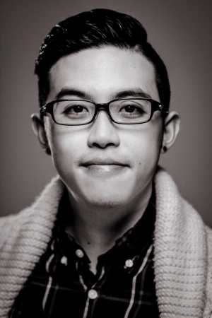 A Chinese American man with black hair dressed in a plaid shirt and cable-knit sweater.