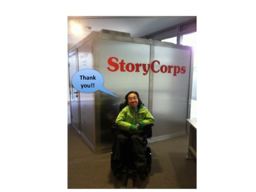 Asian American woman wearing a green rain jacket in a wheelchair in front of a large cubical recording booth with the word 'StoryCorps' in front. A caption bubble reads, "Thank you!!"